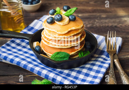 Pila di Pancake fatti in casa nella padella di ferro con mirtilli, banana e foglie di menta sul legno rustico sfondo. Foto Stock