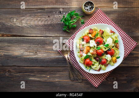 Fettuccine con pomodori al forno, pancetta e formaggio mozzarella su legno rustico sfondo. Vista dall'alto. Foto Stock