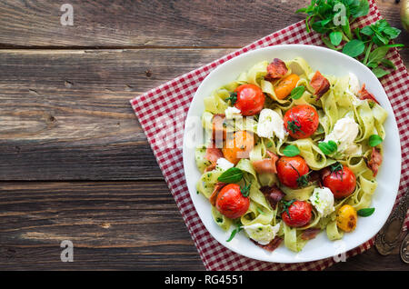 Fettuccine con pomodori al forno, pancetta e formaggio mozzarella su legno rustico sfondo. Vista dall'alto. Foto Stock