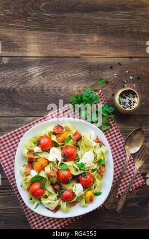 Fettuccine con pomodori al forno, pancetta e formaggio mozzarella su legno rustico sfondo. Vista dall'alto. Foto Stock