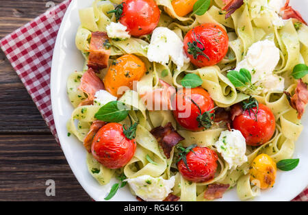 Fettuccine con pomodori al forno, pancetta e formaggio mozzarella su legno rustico sfondo. Vista dall'alto. Foto Stock