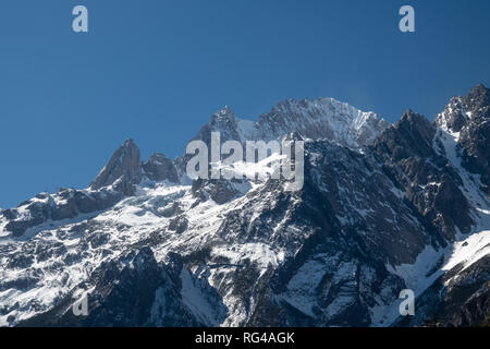 Jade dragon snow mountain situato in Yulong, Yunnan in Cina. Montagne coperte di neve con picchi rocciosi con alberi in primo piano dando una drammatica Foto Stock