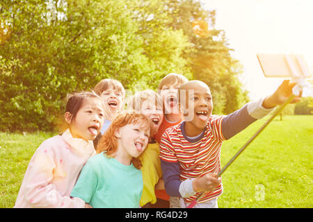 Gruppo di bambini nel parco è rendere selfie con lo smartphone su selfie stick Foto Stock