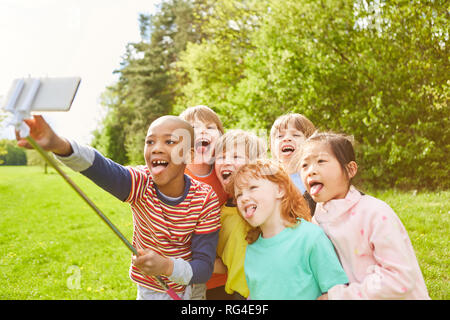 Gruppo di bambini prende un selfie con lo smartphone e selfie stick, mostrando la loro lingua Foto Stock