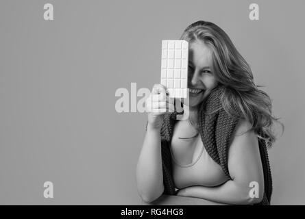 Felice giovane bella donna di mangiare il cioccolato bianco. Giovane biondo con trucco naturale divertendosi e mangiando cioccolato. Foto Stock