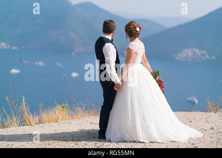 Agli sposi novelli stare su un palco e tenendo le mani sguardo sul mare Foto Stock