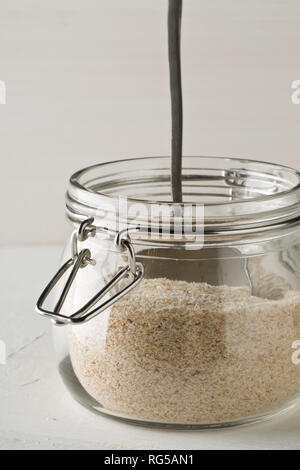 Accumulo di pula di psillio anche chiamato isabgol nel vasetto di vetro con cucchiaio in metallo bianco su sfondo tabella. Psillio lolla anche chiamato isabgol è fibra derivata Foto Stock