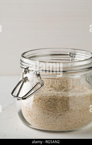 Accumulo di pula di psillio anche chiamato isabgol nel vasetto di vetro sul tavolo bianco sullo sfondo. Psillio lolla anche chiamato isabgol è fibra derivata da semi di Foto Stock