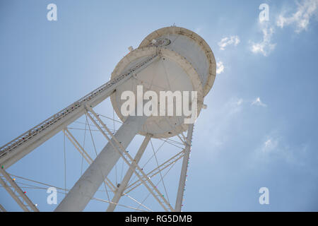 Guardando verso l'alto un bright white water tower da sotto retroilluminata con il sole e un luminoso cielo blu. Foto Stock