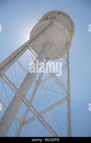 Guardando verso l'alto un bright white water tower da sotto retroilluminata con il sole e un luminoso cielo blu. Foto Stock