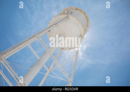 Guardando verso l'alto un bright white water tower da sotto retroilluminata con il sole e un luminoso cielo blu. Foto Stock