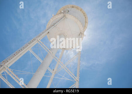 Guardando verso l'alto un bright white water tower da sotto retroilluminata con il sole e un luminoso cielo blu. Foto Stock