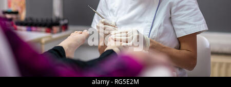 Ampia vista immagine di una donna seduta in confortevole sedia cosmetici ottenendo una pedicure da un professionista estetista. Foto Stock