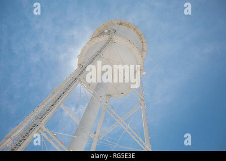 Guardando verso l'alto un bright white water tower da sotto retroilluminata con il sole e un luminoso cielo blu. Foto Stock