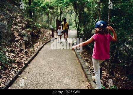 Una ragazza saldi su un percorso di pietra mentre si cammina dietro la sua famiglia, felce piatta zona campeggio, Eungella National Park, Queensland, Australia Foto Stock