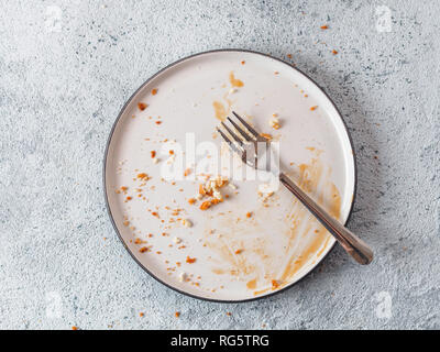 Vuoto piatto sporco dopo la cheesecake con salsa di caramello e dessert forcella. Rustico bianco moderno e alla moda quartiere alla moda di sporco sulla piastra di cemento grigio Sfondo, vista dall'alto piatto o laici. Copia spazio per il testo Foto Stock