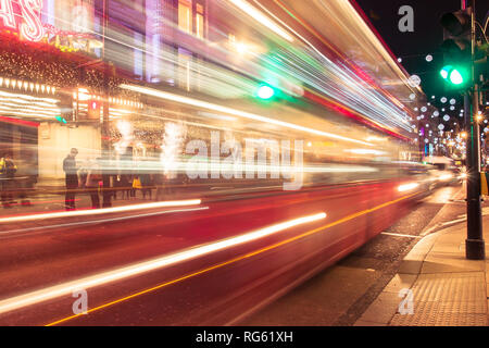Sfocata London bus rosso attraversando Oxford Street con i pedoni in attesa al semaforo Foto Stock