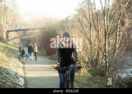 Donna in bicicletta lungo un sentiero lungo il fiume, Germania Foto Stock