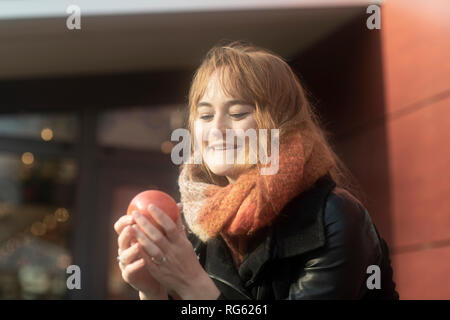 Donna sorridente in piedi all'aperto tenendo un apple, Germania Foto Stock