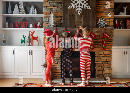 Tre bambini appendere le calze di Natale su un caminetto Foto Stock