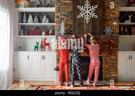 Tre bambini appendere le calze di Natale su un caminetto Foto Stock
