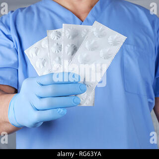 Medico di guanti in lattice blu pillole tiene in carta bianca imballaggio, close up Foto Stock