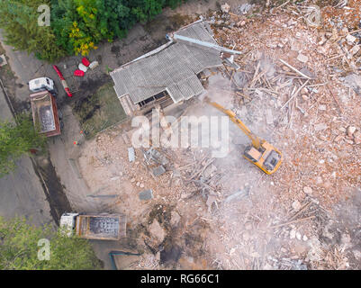 Escavatore giallo sul sito di demolizione lavorando sul vecchio edificio e carico dei detriti in autocarri a cassone ribaltabile. vista aerea Foto Stock