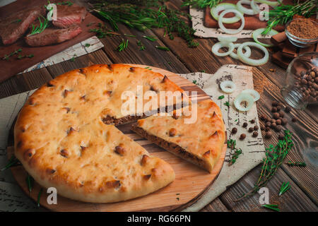 Ossezi torta a base di carne di manzo con su un sfondo di legno con ingredienti. La cottura tradizionale concetto con spazio di copia Foto Stock