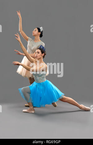 Vista laterale della bella ballerini indossano abiti e corone sollevando in alto le mani e guardando al di sopra. Due giovani ballerina in posa sul grigio Sfondo isolato in studio. Concetto di arte classica Foto Stock