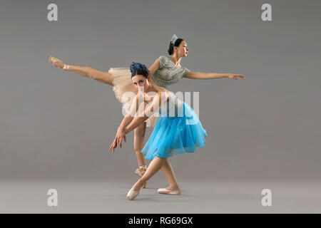 Due ballerine professioniste di indossare abiti e scarpe da ballo danza su sfondo grigio in studio. Femmina grave flessione verso il basso e guardando la telecamera mentre il partner in piedi su una gamba dietro. Foto Stock