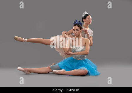 Graziosa ballerina seduta sul pavimento e guardando la telecamera mentre partner femmina seduto sul ginocchio dietro e sollevando una gamba. Due artisti professionisti che pongono in studio. Concetto di balletto e arte. Foto Stock