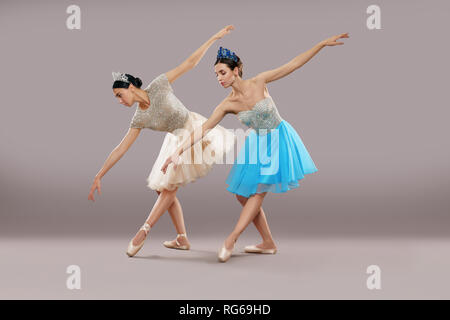 Vista laterale di due ballerini professionali in abiti, scarpe da ballo e danza corone e la piegatura verso il basso in studio. Slim ballerine di eseguire sul grigio Sfondo isolato. Concetto di arte classica". Foto Stock