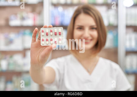 Il farmacista femmina holding e mostrando in blister. Close up di pillole. Felice farmacista vendita di medicinali. La donna in bianco uniforme sorridente, guardando la fotocamera e in posa. Foto Stock