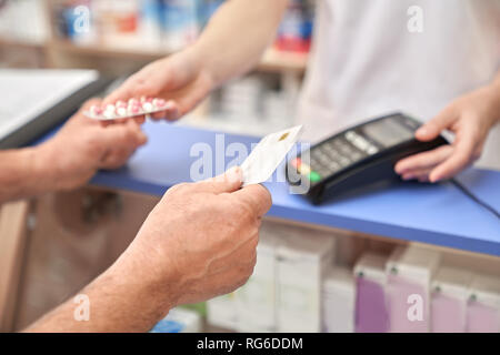 Uomo che mostra carta di credito dopo aver effettuato l'acquisto tramite il terminale. Macchina di pagamento sul contatore in farmacia. Il farmacista dando blister di pillole per il cliente. Foto Stock