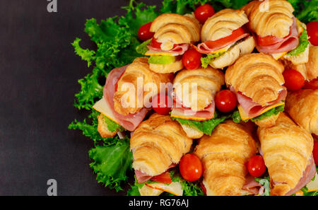 Croissant fresco o in sandwich con insalata, prosciutto cotto, prosciutto, pomodori su sfondo di legno prima colazione al mattino concept Foto Stock