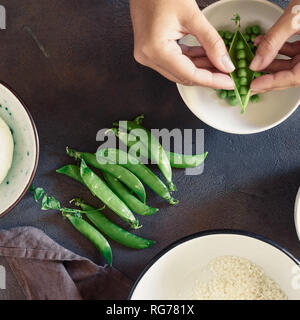 Mani femminili preparare vegetariano risotto con piselli verdi, menta e formaggio di capra. Cibo sano concetto. Materie prime per la cottura risotto vista superiore Foto Stock