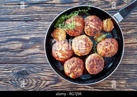 In casa la carne fritta cotolette, polpette di carne tritata in una padella con il timo, aglio e cipolla su un vecchio tavolo di legno, vista da sopra, close-up Foto Stock