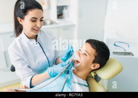 Guarnizione di tenuta del processo di installazione, odontoiatria pediatrica, bambini stomatologia. Dentista femmina denti di perforazione, clinica dentale Foto Stock