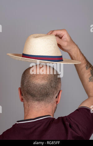 Balding uomo a mettere su un cappello di paglia per la protezione solare. Foto Stock