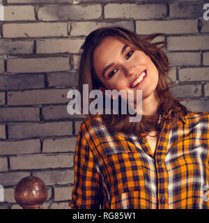 Bella toothy positivo donna sorridente cercando felice nel casual maglietta arancione e blu jeans sul blu di mattoni di sfondo per studio. Tonica closeup Foto Stock