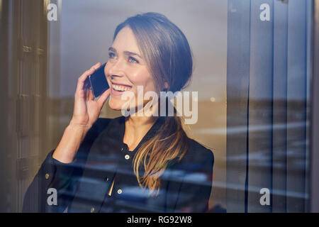 Ritratto di ridere imprenditrice sul telefono dietro il vetro di finestra Foto Stock