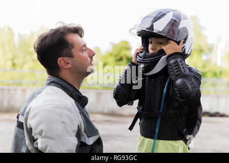 Padre guardando figlio mettendo sul casco del motociclo Foto Stock