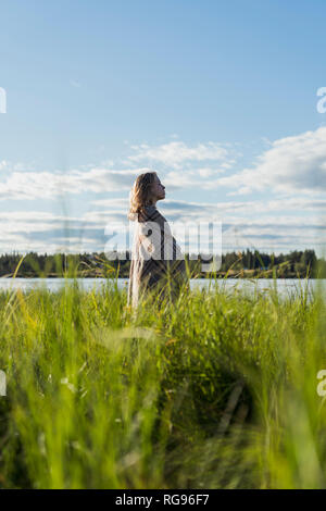 Finlandia, Lapponia, donna avvolta in una coperta in piedi sulla riva del lago Foto Stock