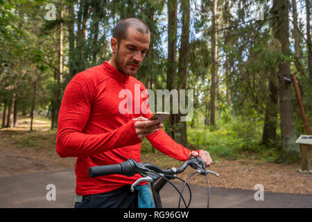 Mountain Biker utilizza lo smartphone in una foresta Foto Stock