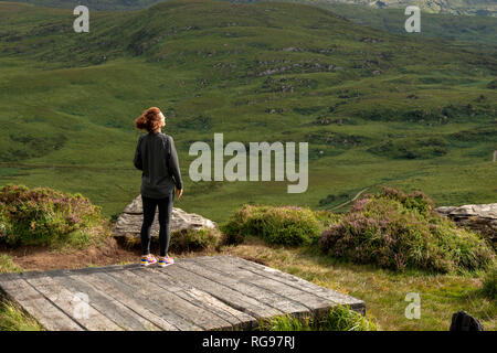 Giovane ragazza escursionista sulla piattaforma panoramica ammirando la vista panoramica della Old Kenmare Road dal sentiero escursionistico di montagna Troc a Killarney, Irlanda Foto Stock