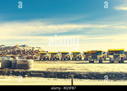 Il grande giallo autocarri a cassone ribaltabile sono messi in linea nella miniera con la vecchia cava di data mining e il cielo blu con nuvole in background Foto Stock