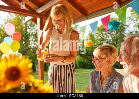 Donna felice che serve succhi di frutta su un party in giardino Foto Stock