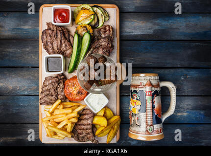 La birra snack set. Set di carne servita sul tagliere con la tazza di antiquariato, sullo sfondo di legno. Foto Stock