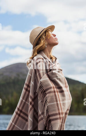 Finlandia, Lapponia, donna che indossa un cappello avvolto in una coperta permanente al lago Foto Stock