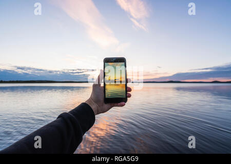 Finlandia, Lapponia, uomo prendendo cellulare foto del bellissimo lago al crepuscolo Foto Stock
